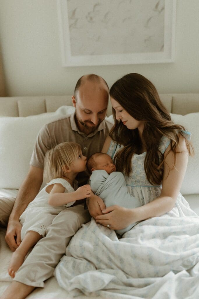 child kissing newborn baby's head in lifestyle photoshoot