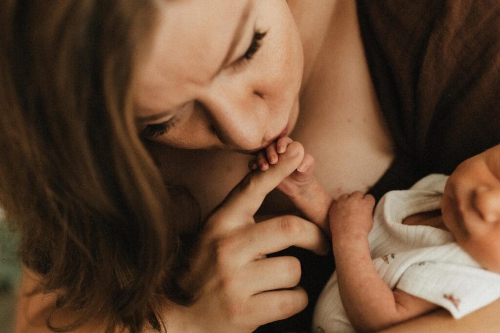 mom kissing baby's finger during newborn photo session
