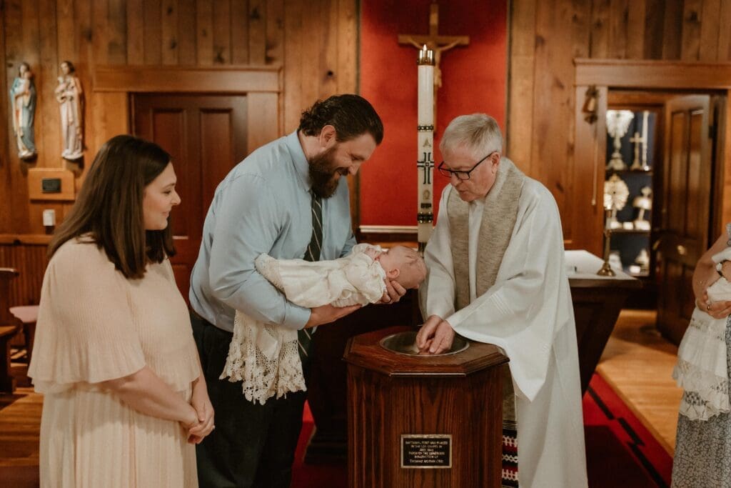 Parents holding baby during baptism at Notre Dame Log Chapel