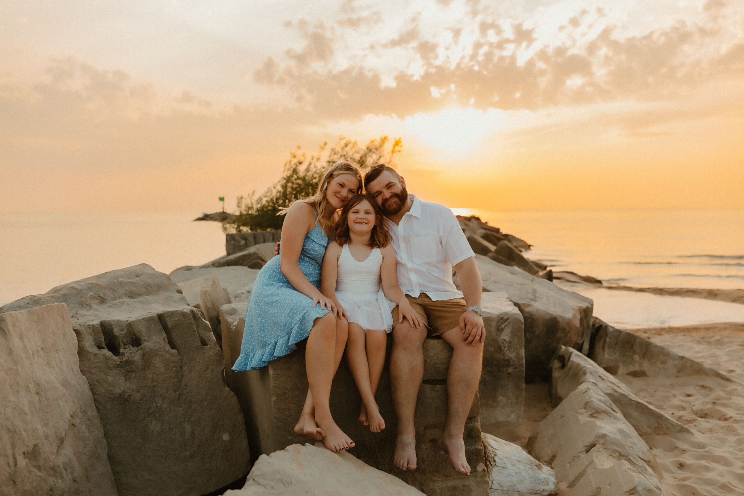 family sits on rocks during sunset golden hour beach photography session in south haven michigan