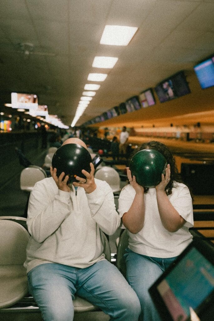 engaged couple holding up bowling balls for posed portrait in alley 