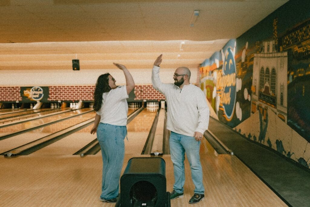 creative engagement session at bowling alley of couple with hands in air giving high fives 