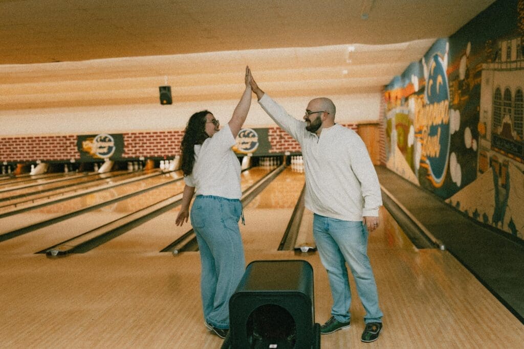 creative and fun candid photo of couple high five after strike in bowling alley engagement session