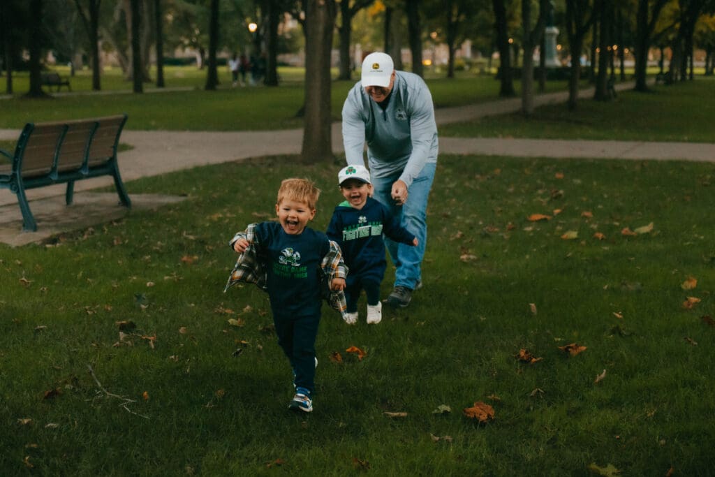 Three-photo sequence of a grandfather running behind his laughing grandsons on the grass.