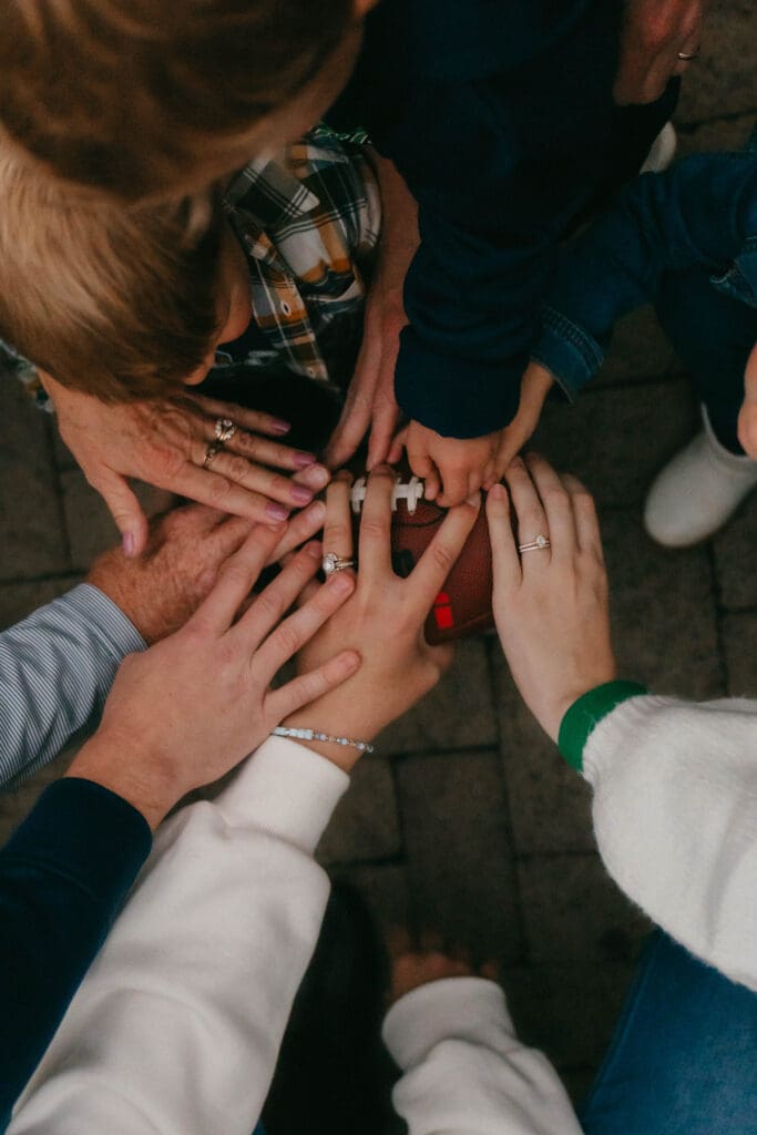 Adults’ and children’s hands gathered together around a small football.